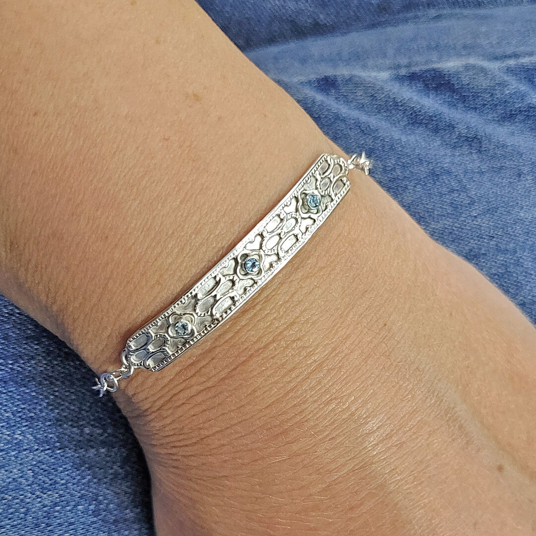 Close up of geometric detail and blue topaz stones of sterling silver bar bracelet worn on wrist 