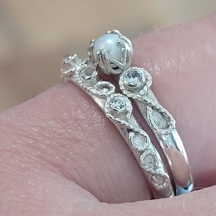 Close-up of detail on Vintage style scrollwork pearl and white sapphire engagement ring and matching scrollwork white sapphire wedding band bridal ring set in sterling silver 